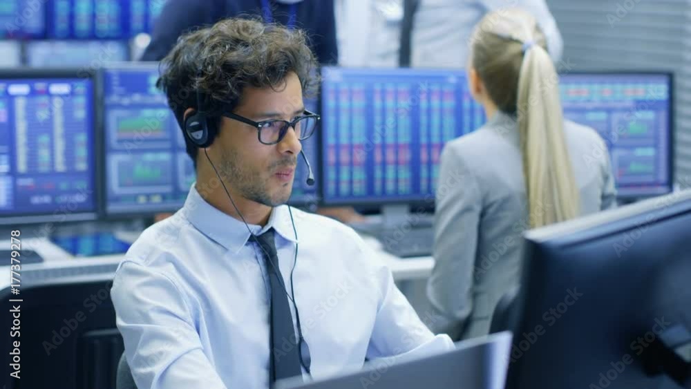 Aufkleber Stock Trader Making Sales with a Headset. In the Background Stock Exchange Office and Group of Traders Working at their Workstations.
