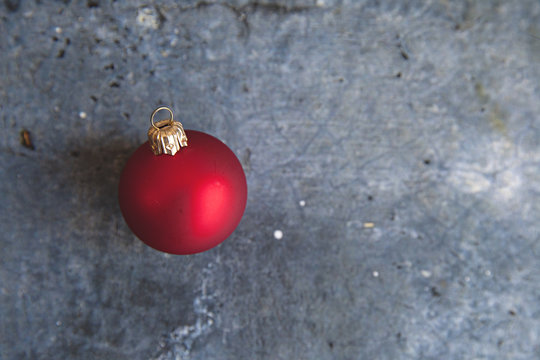 bright red Christmas bauble sits atop of a concrete textured background