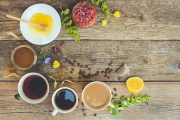     Tea, coffee, cocoa in cups, chicory, lemon, mint, jam made of rose petals, dried lime, honey on the old wooden background. Toned image. Top view. 