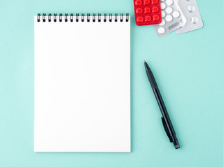 open notebook with blank white clean page to write the treatment plan of the disease. Pills, pen, paper on blue background, top view.