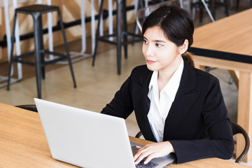 Smiling Beautiful business woman using laptop and looking something with copy space. Business people working with laptop on wood table in coffee shop. Nowadays, we can working at the coffee shop.