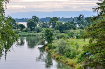 Cloudy summer landscape. Green trees with lakes and mountains in the background.
