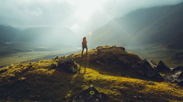 Hiker Young Woman With Backpack Rises To The Mountain Top Against Backdrop Of Sunset. Discovery Travel Destination Concept