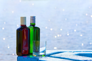 Bottles of whiskey and gin with glass on background of lake