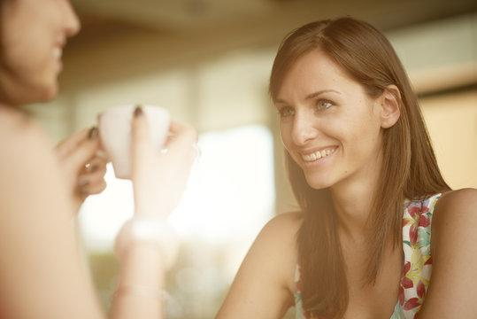 Two Girls Chatting And Drinking Coffee While Sitting In Cafe