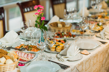 Beautiful festive table served for wedding celebration dinner at home or restaurant interior. Plenty of different food and cutlery. Long table covered with tablecloth and decorated with flowers.