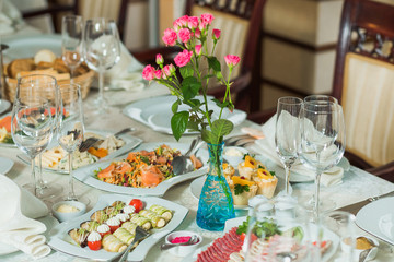 Beautiful festive table served for holiday dinner at home or restaurant interior. Plenty of different food and cutlery on table covered with tablecloth and decorated with flowers.