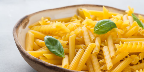 Italian raw short pasta in a dish with basil leaves on gray background