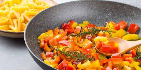 Cooking bell peppers with rosemary in skillet as sauce for italian pasta