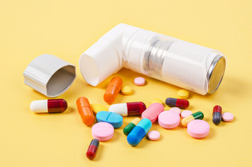White asthma inhaler and colorful pills drug.