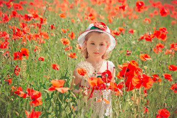 Cute blond young girl child stylish dressed in white handmade hooked dress wearing airy hat top posing on meadow of forest poppy poppies Adoreable scene