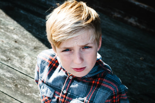 A youth in a plaid shirt sitting on weathered decking.