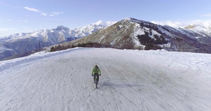 backward aerial over biker man cycling on snowy path during winter with mtb e-bike. Cyclist on bike on snow outdoors in winter. 4k drone flight video