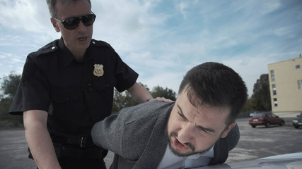 Police officer arresting criminal, putting him on car trunk and reading rights for him.