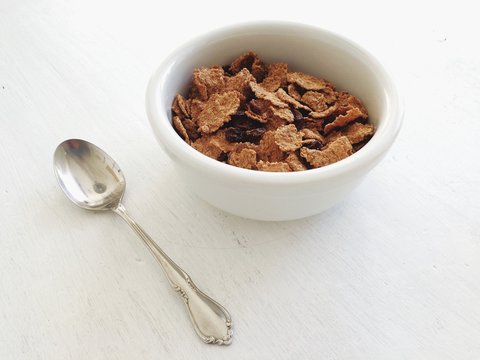 A bowl of fresh breakfast cereal on a white table with a silver spoon