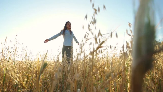 Beautiful girl walking and upping her arms in a wheat field with the sun behind