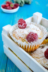 Curd cakes (muffins) with raspberries, decorated with powdered sugar. Serve in a white wooden box. Fresh raspberries in a ceramic bowl.