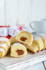 Homemade croissants with fruit jam, decorated with powdered sugar with a cup of morning tea on a white wooden background, scattered gift white and red boxes, tied with a twine.