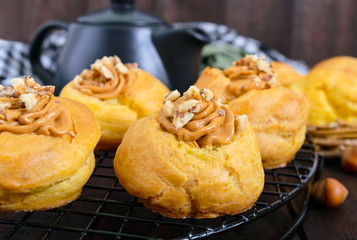 Air profiteroles filled with caramel cream with nuts,  teapot on a dark wooden background.
