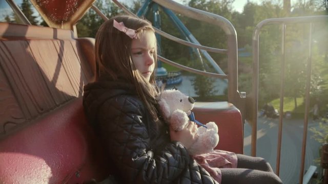Girl with teddy bear in the amusement park in kids train. Children outdoors.