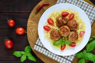 Chicken meat balls, pasta fusilli, tomatoes, basil on a white plate on a wooden tray. Top view.