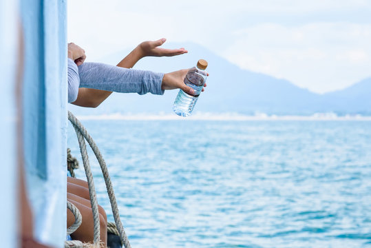 Hand of girl hold a bottle of water in hand hang off edge Passenger boat in ocean.