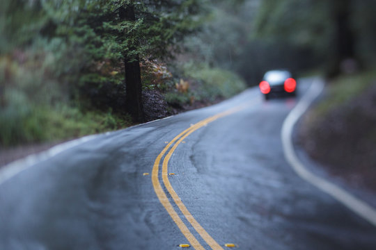 Rainy, curvy wet forest road with car taillights