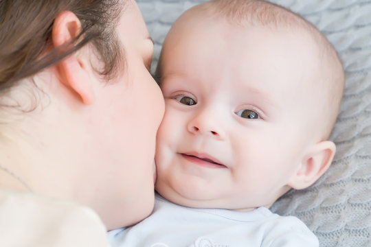 Close-up portrait of happy young mother hugging and kissing his sweet adorable child. Indoors shot, concept image