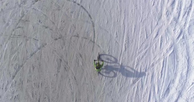 overhead aerial over biker man cycling on snowy path during winter with mtb e-bike. Cyclist on bike on snow outdoors in winter. 4k top view drone flight video