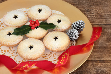 Christmas mince pies with holly and red ribbon on a gold plate on oak wood table background.