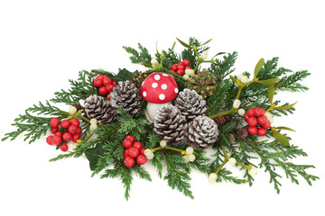 Christmas fantasy table decoration with fly agaric mushroom, holly, ivy, mistletoe, cedar and juniper leaf sprigs and pine cones on white background.