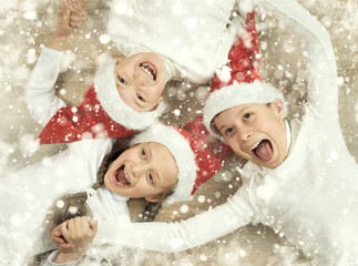 happy child lying together on wooden background, dressed in christmas Santa hat and having fun, winter holiday concept, snow decoration, yellow toned