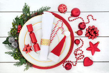 Christmas dinner table setting with porcelain plates, serviette, red decorations with holly,...