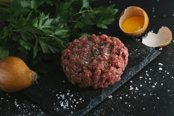 Tartare steak. Beef raw chopped meat with spices, herbs and egg yolk. Fresh, spicy, delicious, gourmet meal on dark background with copy space, close-up.