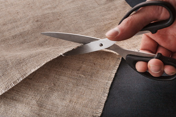 A man's hand cuts linen cloth with tailor's scissors.