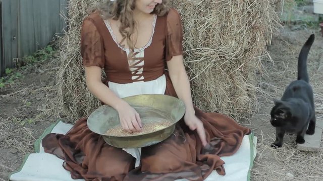 beautiful woman in a rustic dress sits on a hay and sifts the grain
