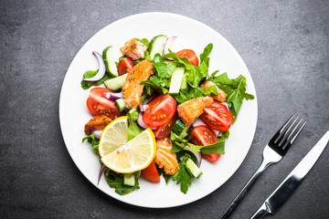 Fresh salad with salmon and vegetables on black background.