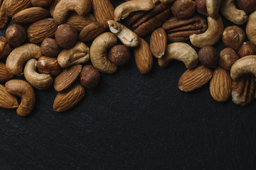 Variety of mixed nuts - almond, hazelnuts and cashew - on the dark slate background with copy space. Top view. Toned