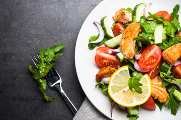 Fresh salad with salmon and vegetables on black background.
