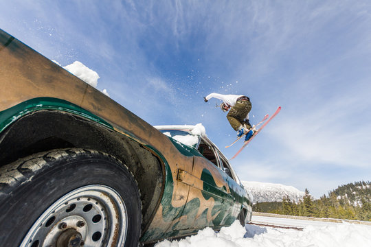 Ski freestyle - Skier jumping over old abandoned racing car from a low angle point of view