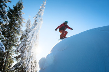 Freeride snowboarder riding on dangerous slope. Blue sky and sun on the background copyspace