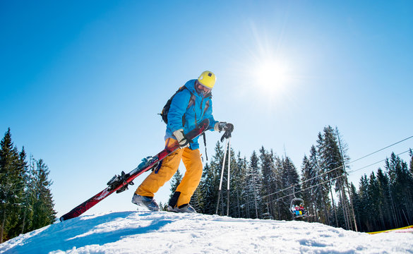 Male skier walking up the snowy hill in the mountains carrying his ski equipment. Beautiful sunny winter day copyspace nature active lifestyle winter resort leisure concept