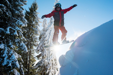 Snowboarder flying in the air while skiing on the slope in the mountains. Sun and blue sky on the...