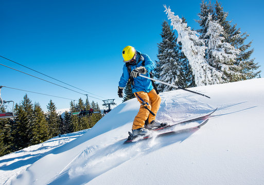Shot of a professional freeride skier riding down in the Carpathians mountains at winter resort on a sunny day. Blue sky and winter forest on the background