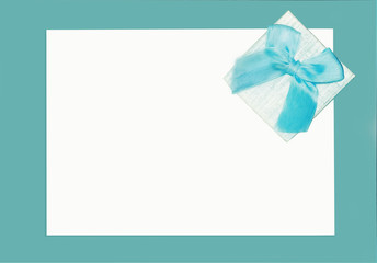 Congratulatory white card lies on a turquoise background. The gift is decorated with a blue ribbon. Lovely woman's card for festive text