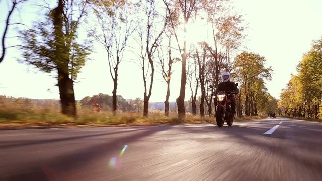 Steadycam shot of motorcyclist driving his motorbike on the road during sunset