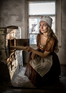 woman in a rustic dress sitting next to old stove in a ruined abandoned house