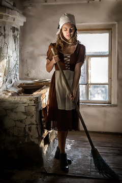 woman in a rustic dress sweeps the wooden floor in the kitchen