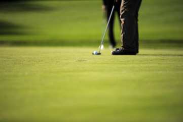 Putting a golf ball into the hole on the green. Focus in the hole.