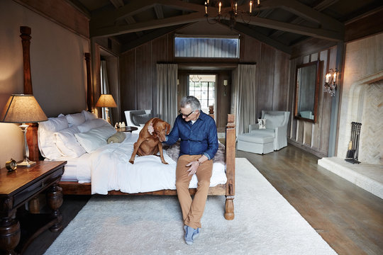 Mature man with grey hair relaxing with his dog in bedroom